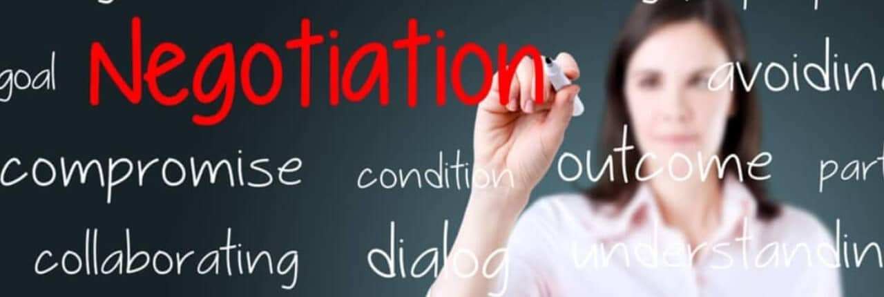 Woman stands behind a glass marker board and writes Negotiation in red.